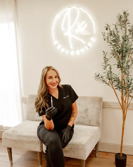 Rhegan Blackerby in black scrubs, seated beneath the illuminated Rx Aesthetics sign.